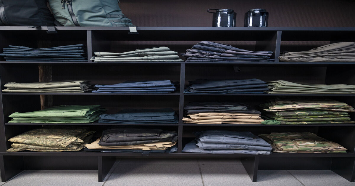 A shelf with stacks of military uniforms in different colors, such as light blues and camouflage.